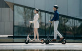 Xiaomi Mi Electric Scooter 3, elektrinis paspirtukas (įvairių spalvų) - Šoninis vaizdas su dviem paspirtukais ir žmonėmis